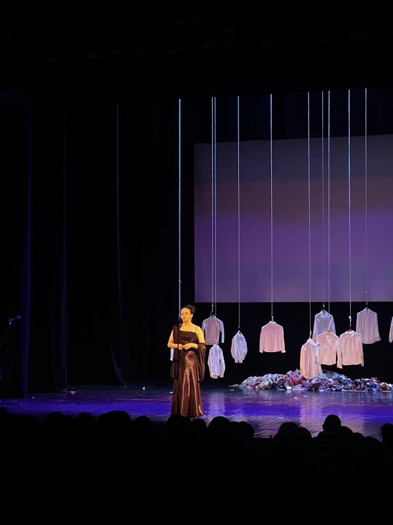 Dziewczyna w eleganckiej długiej sukience stoi na scenie.