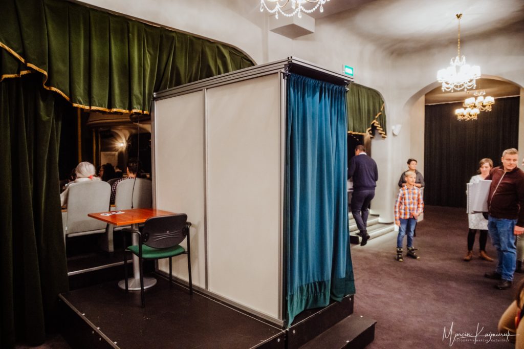 We foyer teatru budka dla lektora audiodeskrypcji na podeście.