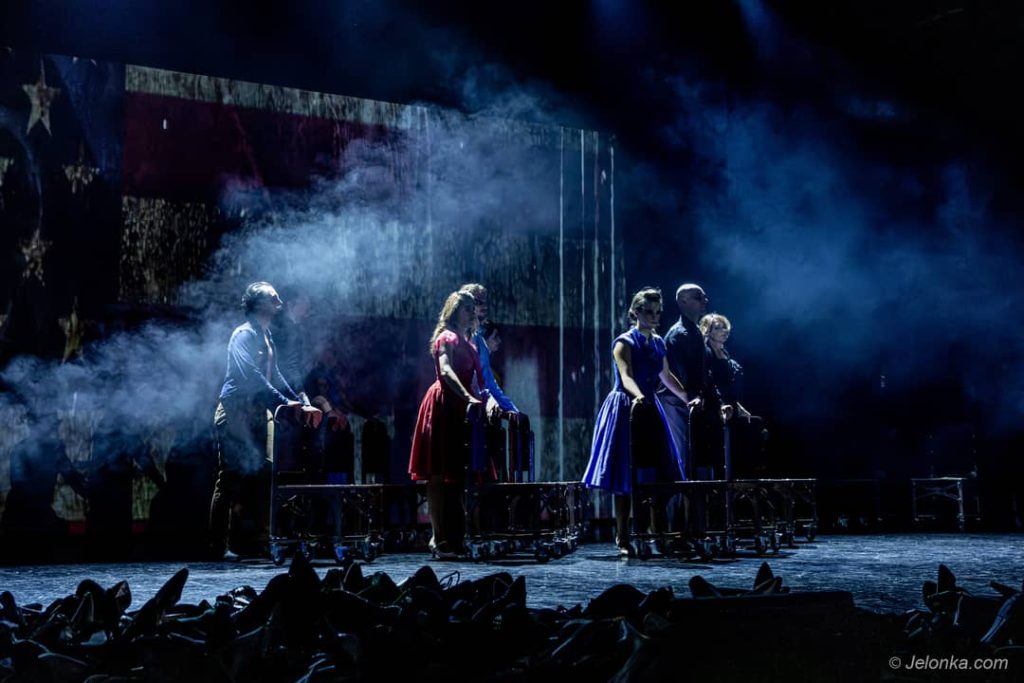 Grupa osób tańcząca na zadymionej scenie.