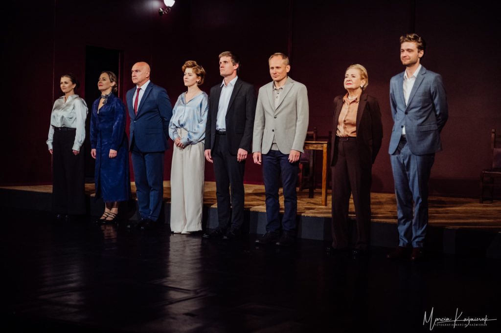 Grupa osób elegancko ubrana stojąca na scenie.