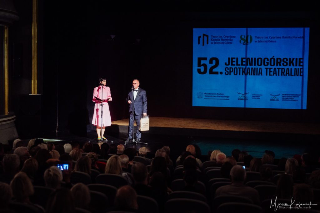 Kobieta i mężczyzna elegancko ubrani stojący na scenie przez publicznością.