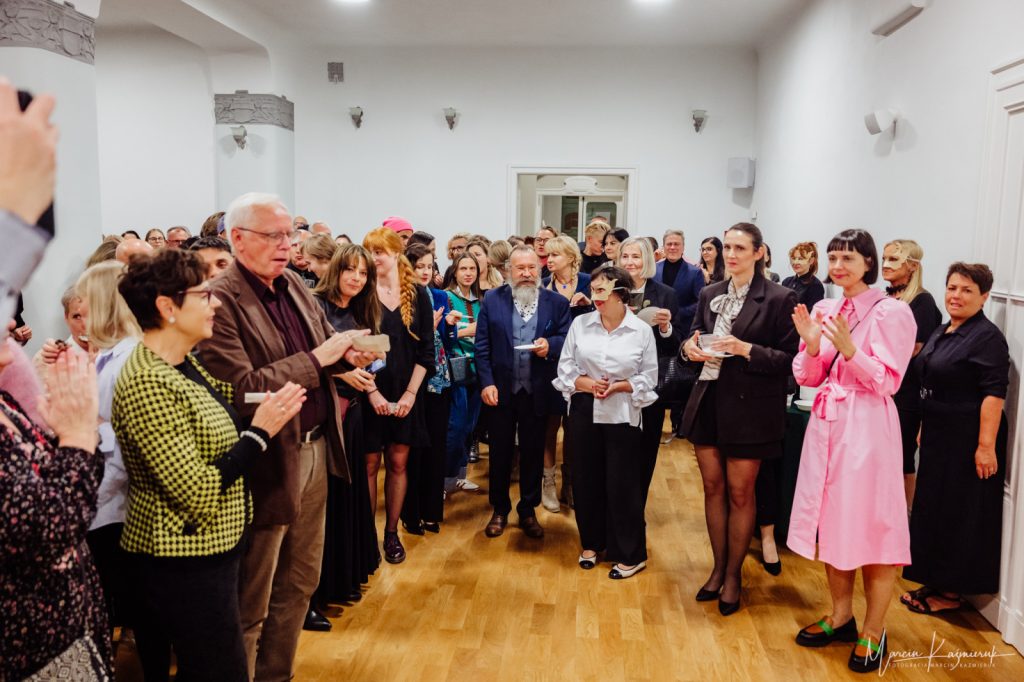 Grupa osób klaszcząca i stojąca w półkole.