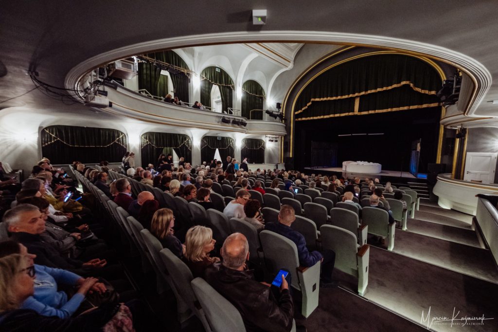 Publiczność siedząca na sali teatralnej, czekająca na rozpoczęcie spektaklu.