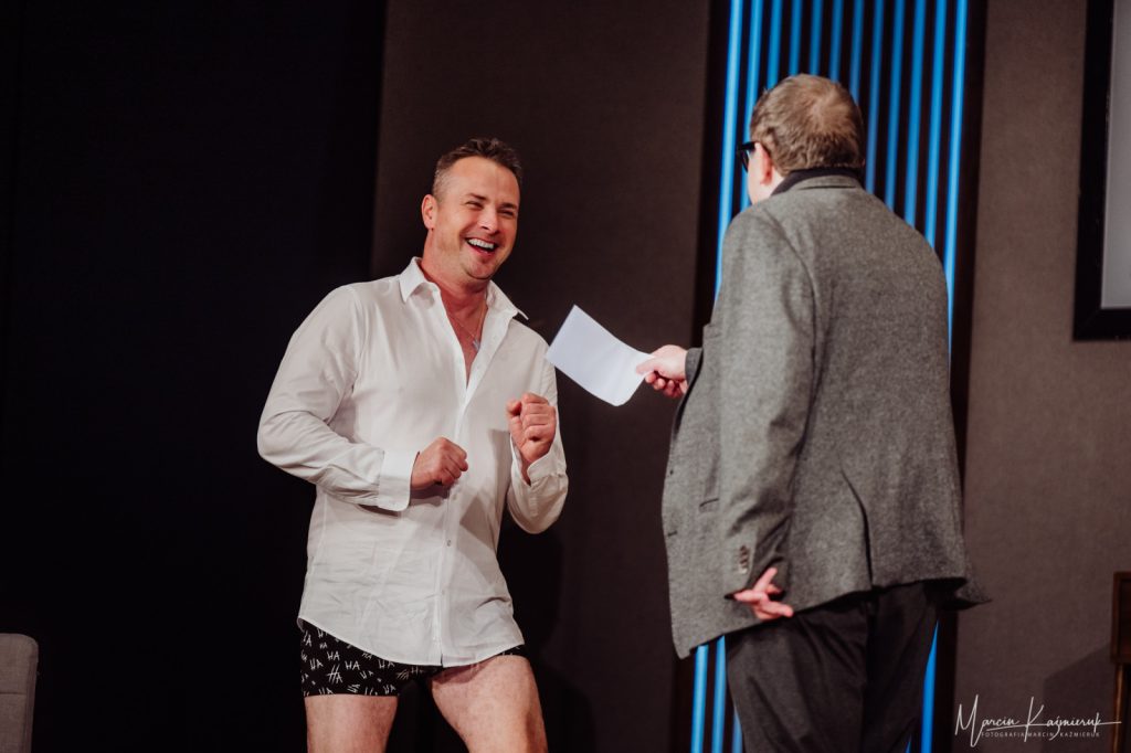 Mężczyzna w szarym garniturze przekazuje kartkę mężczyźnie w białej koszuli.