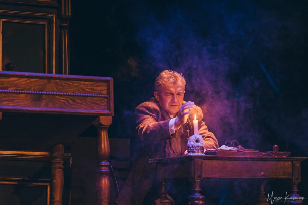 Mężczyzna siedzi przy biurku i zapala świeczkę.