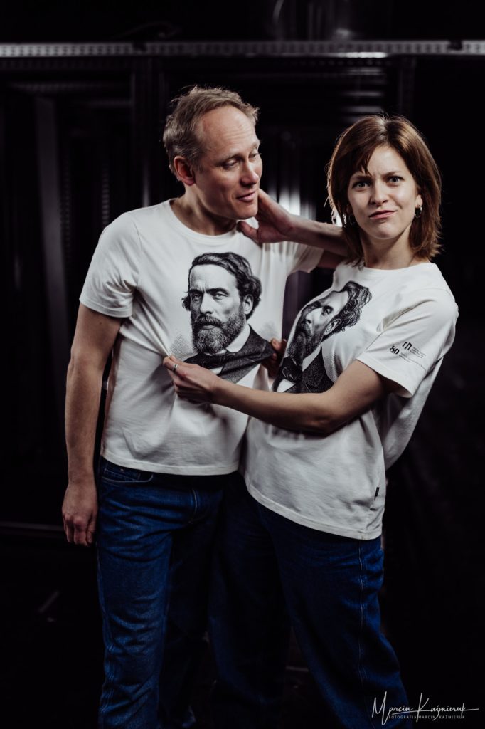 Po lewej stronie mężczyzna, po prawej kobieta, która trzyma go za koszulę. Oboje mają na sobie białe koszulki z wizerunkiem Norwida.