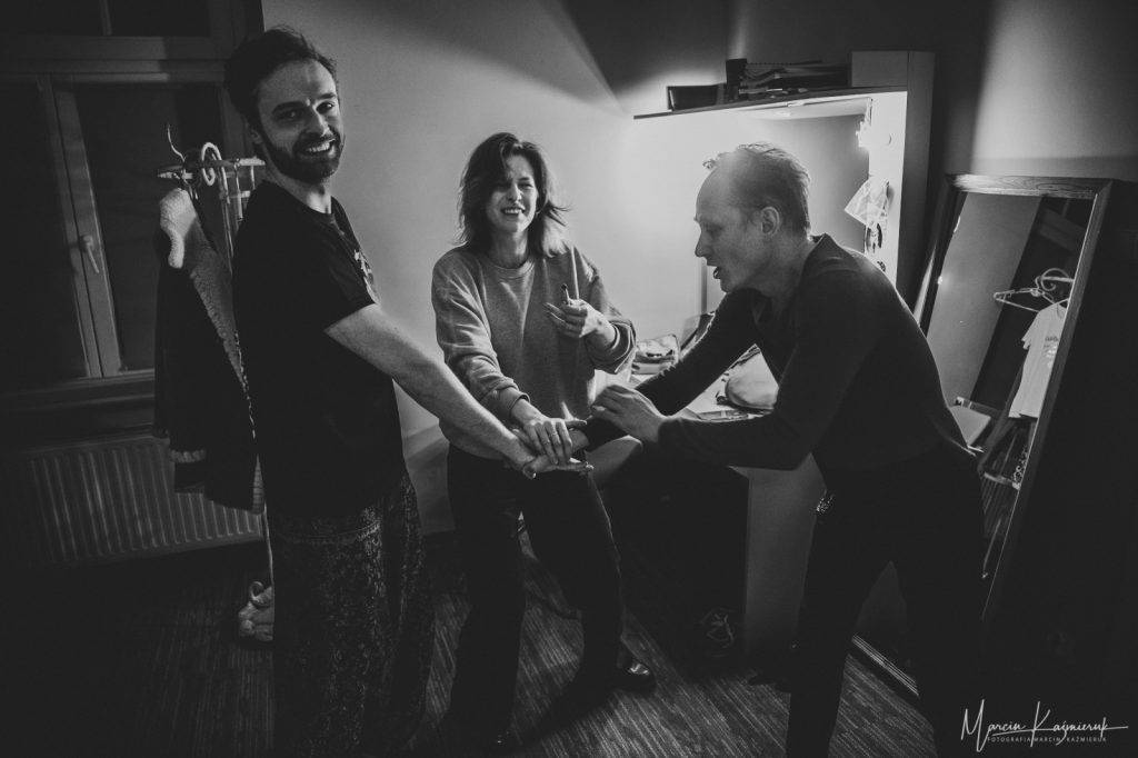 Trzy osoby stoją koło siebie i kładą jedną rękę na drugą.