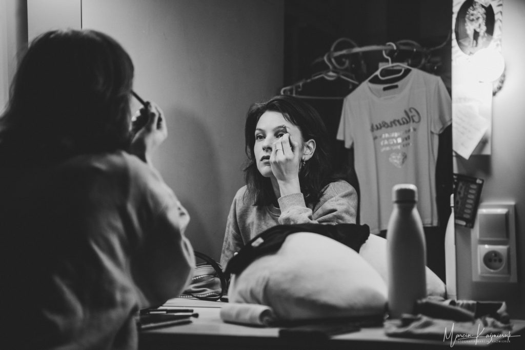 Kobieta siedzi przed dużym lustrem i maluje oczy.