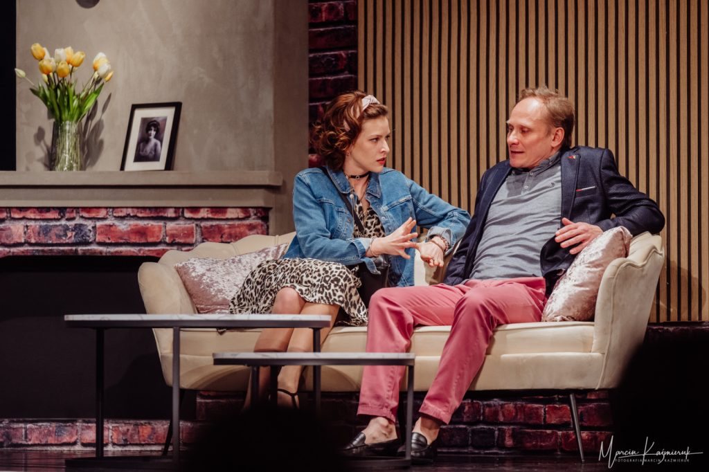 Mężczyzna z kobietą w barwnych strojach siedzą na eleganckiej kanapie.