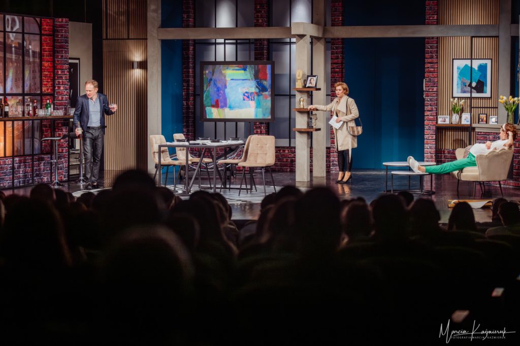 Na pierwszym planie ciemna widownia. W tle scena teatru, a na niej kobieta z mężczyzną.