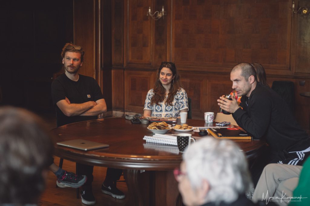 Dwóch mężczyzn, kobieta i starsza pani siedzą i słuchają.