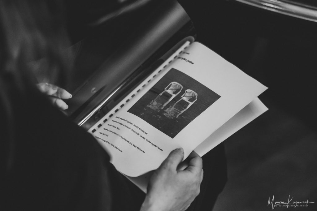 Mężczyzna trzymający folder z kartkami, na jednej z nich widzimy zdjęcie dwóch krzeseł.